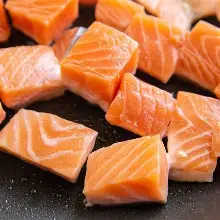 Raw salmon cubes on black skillet